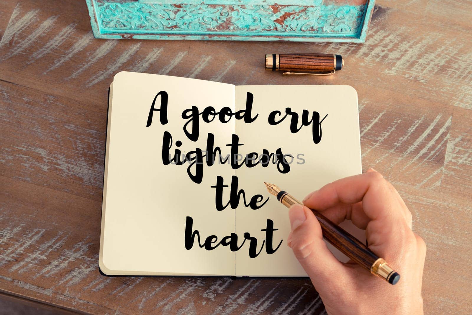 Retro effect and toned image of a woman hand writing on a notebook. Handwritten quote A good cry lightens the heart as inspirational concept image