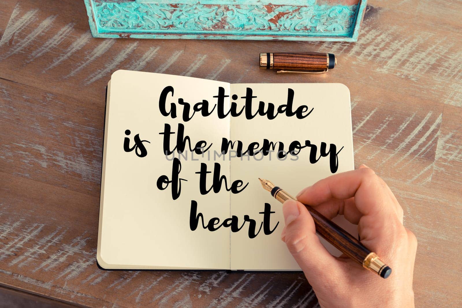 Retro effect and toned image of a woman hand writing on a notebook. Handwritten quote Gratitude is the memory of the heart as inspirational concept image