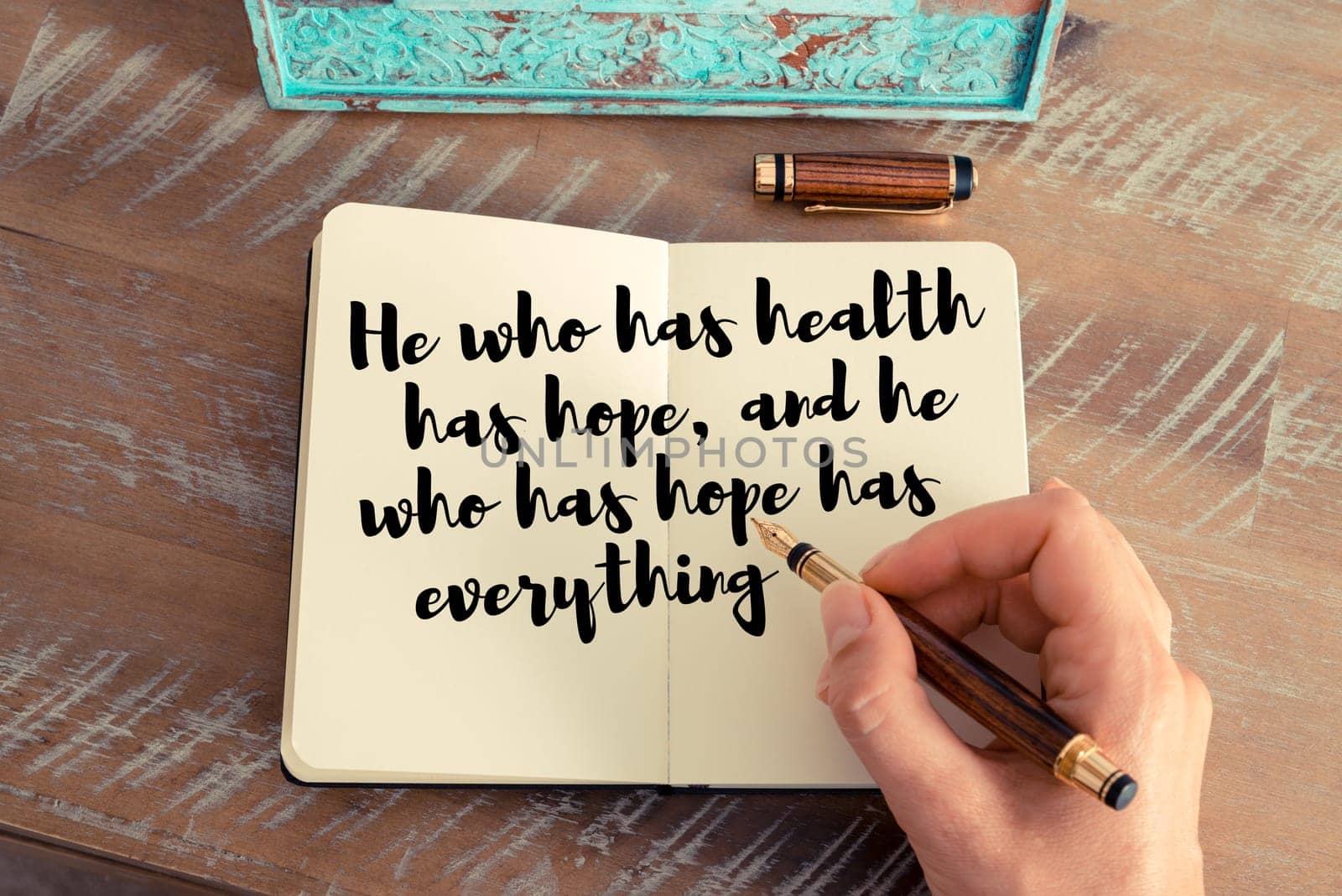 Retro effect and toned image of a woman hand writing on a notebook. Handwritten quote He who has health has hope, and he who has hope has everything as inspirational concept image