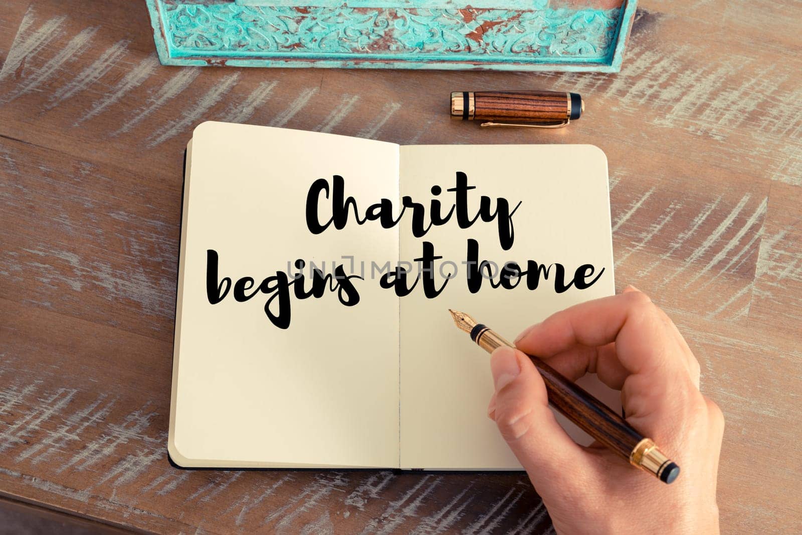 Retro effect and toned image of a woman hand writing on a notebook. Handwritten quote Charity begins at home as inspirational concept image