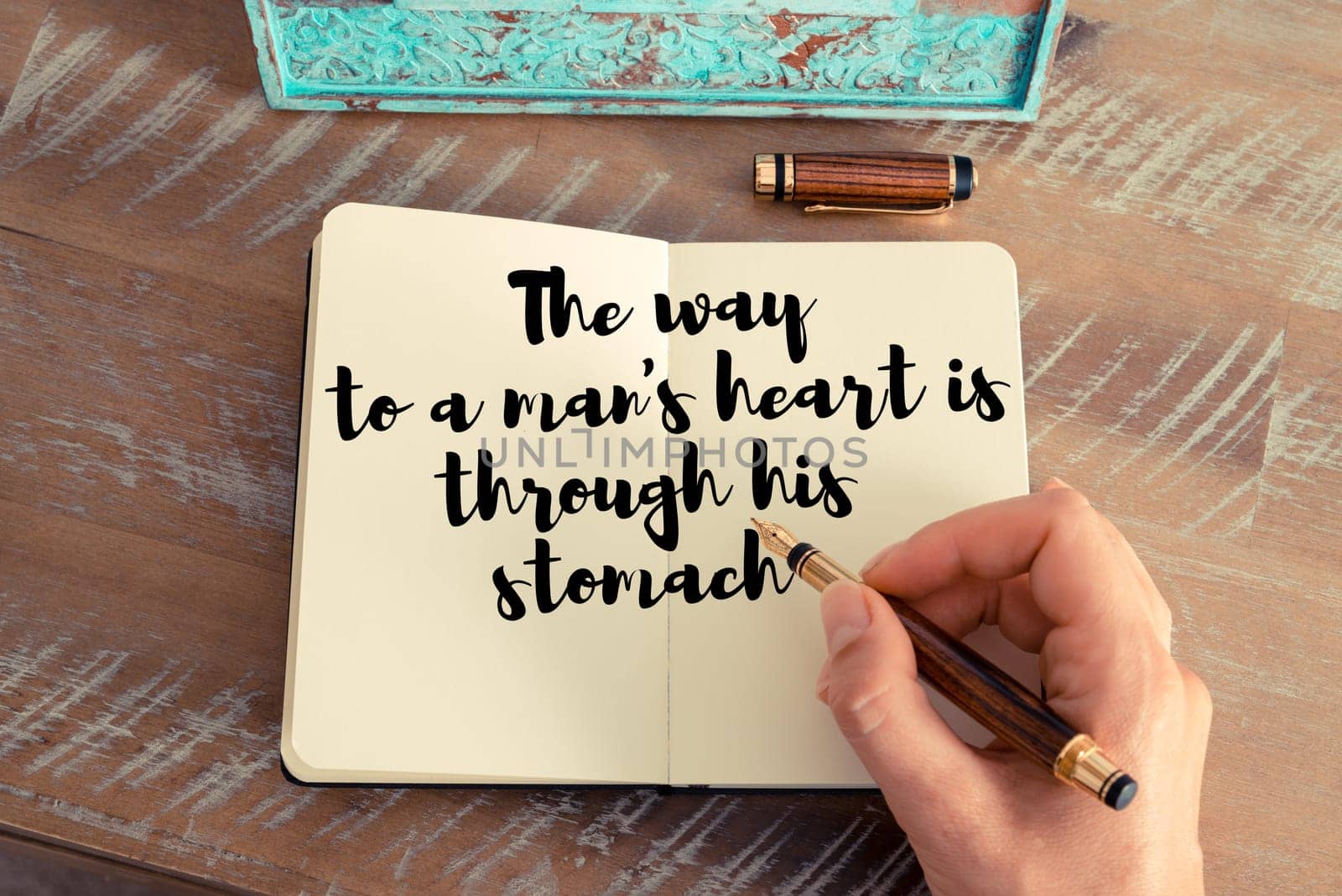 Retro effect and toned image of a woman hand writing on a notebook. Handwritten quote The way to a man&#39 s heart is through his stomach as inspirational concept image
