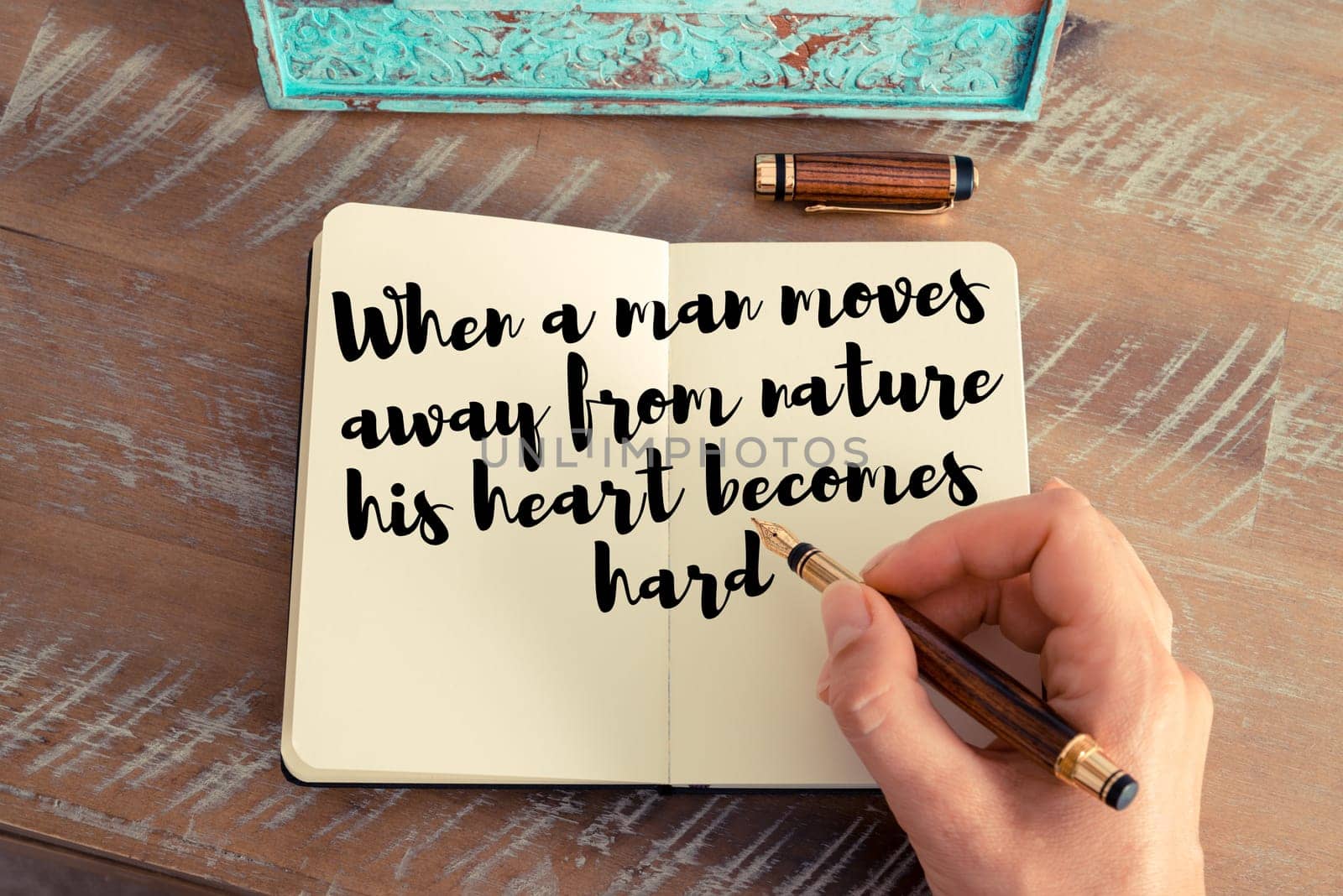 Retro effect and toned image of a woman hand writing on a notebook. Handwritten quote When a man moves away from nature his heart becomes hard as inspirational concept image