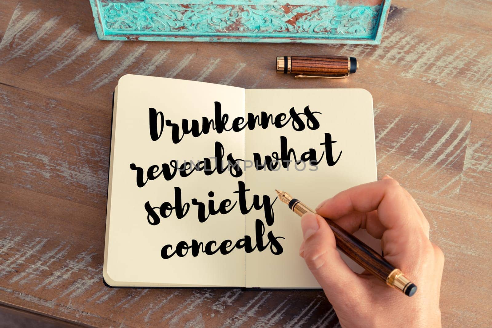 Retro effect and toned image of a woman hand writing on a notebook. Handwritten quote Drunkenness reveals what sobriety conceals as inspirational concept image