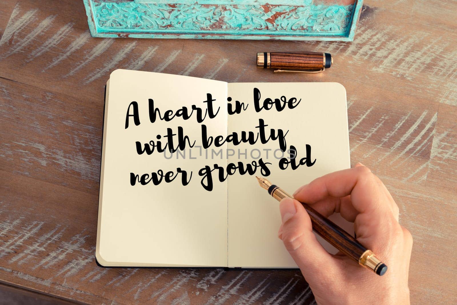 Retro effect and toned image of a woman hand writing on a notebook. Handwritten quote A heart in love with beauty never grows old as inspirational concept image