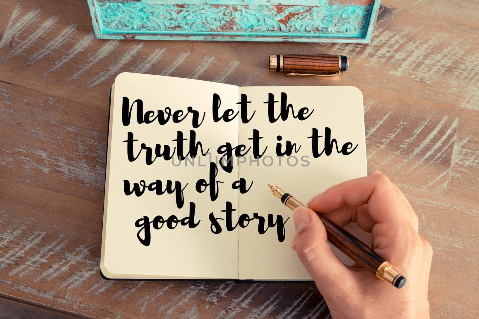 Retro effect and toned image of a woman hand writing on a notebook. Handwritten quote Never let the truth get in the way of a good story as inspirational concept image