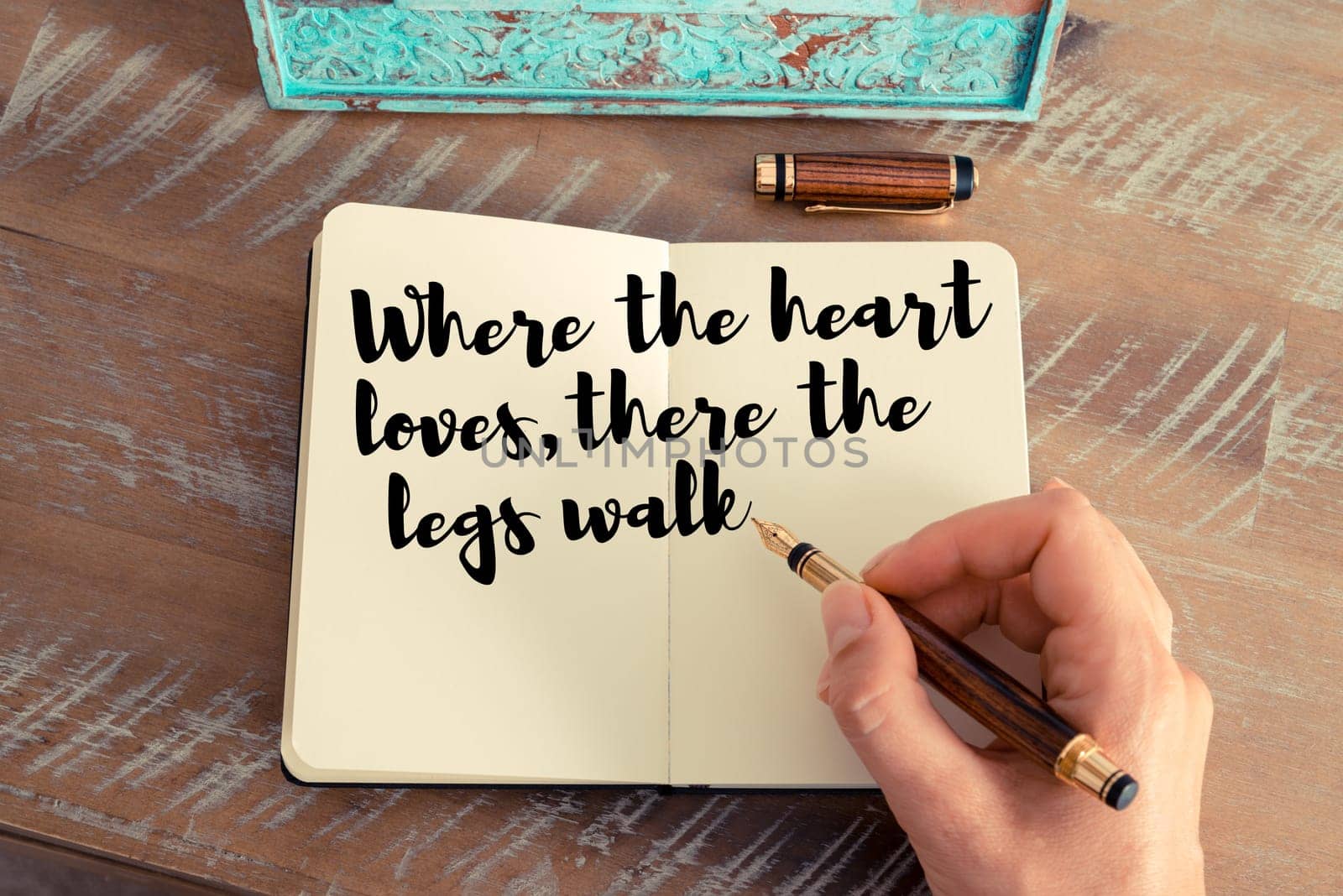Retro effect and toned image of a woman hand writing on a notebook. Handwritten quote Where the heart loves, there the legs walk as inspirational concept image