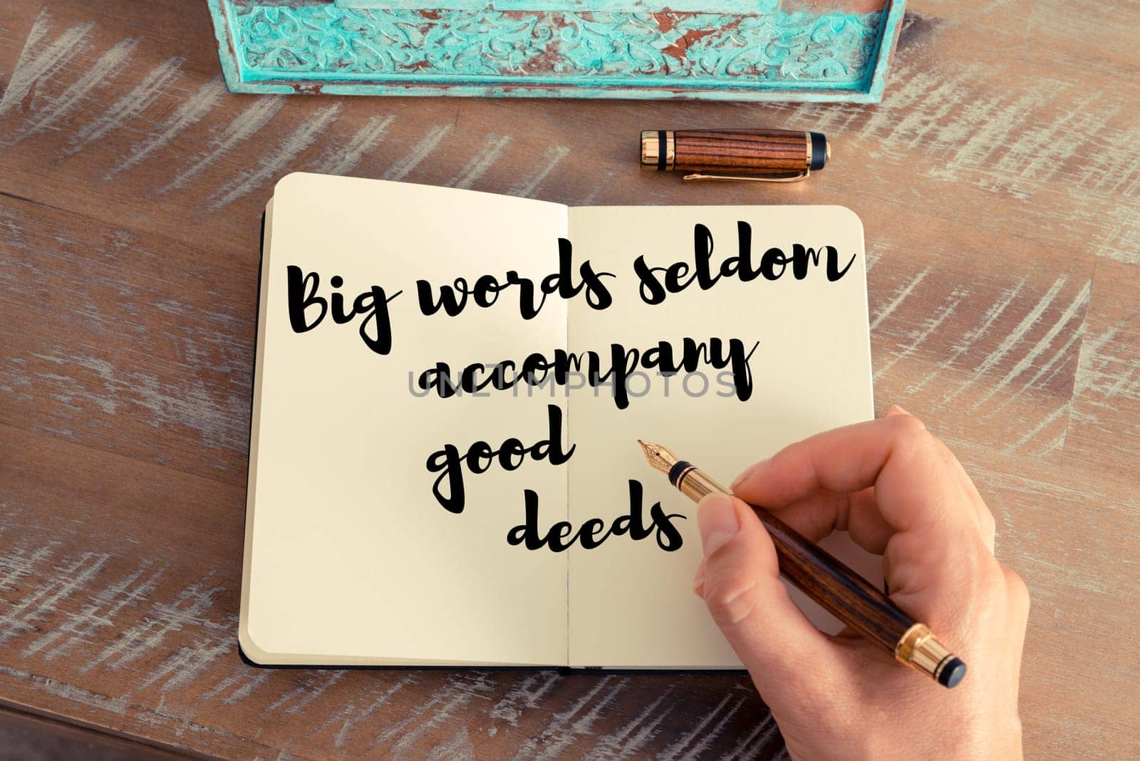 Retro effect and toned image of a woman hand writing on a notebook. Handwritten quote Big words seldom accompany good deeds as inspirational concept image