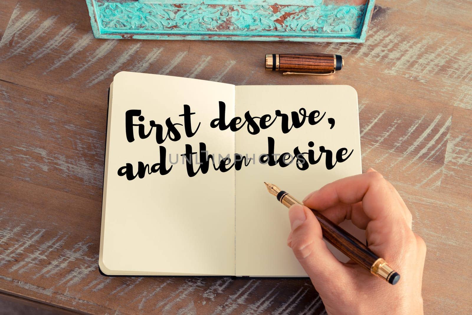 Retro effect and toned image of a woman hand writing on a notebook. Handwritten quote First deserve, and then desire as inspirational concept image