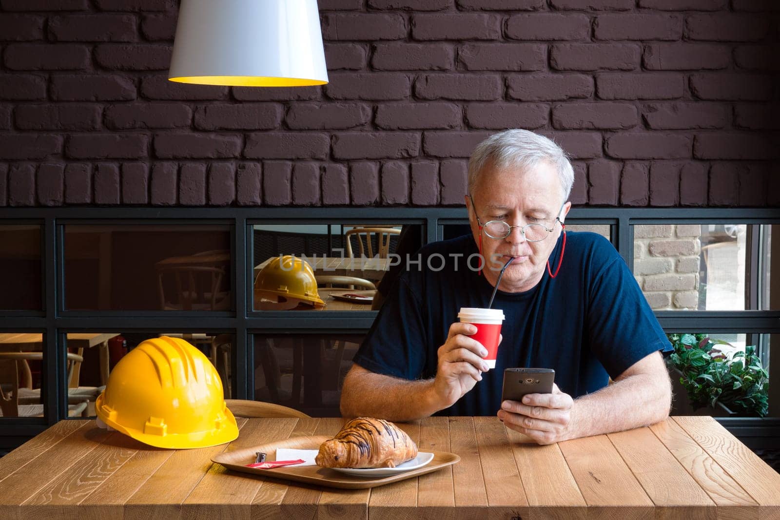 Senior construction foreman taking refreshment break, drinking coffee and checking his phone