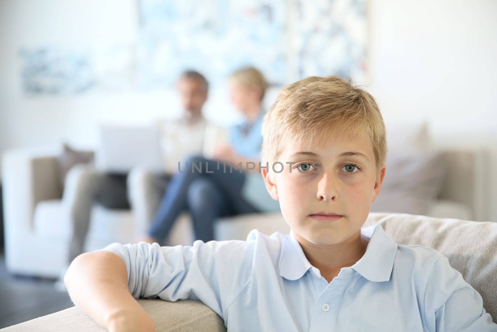 12-year-old boy sitting in couch at home, parents in background