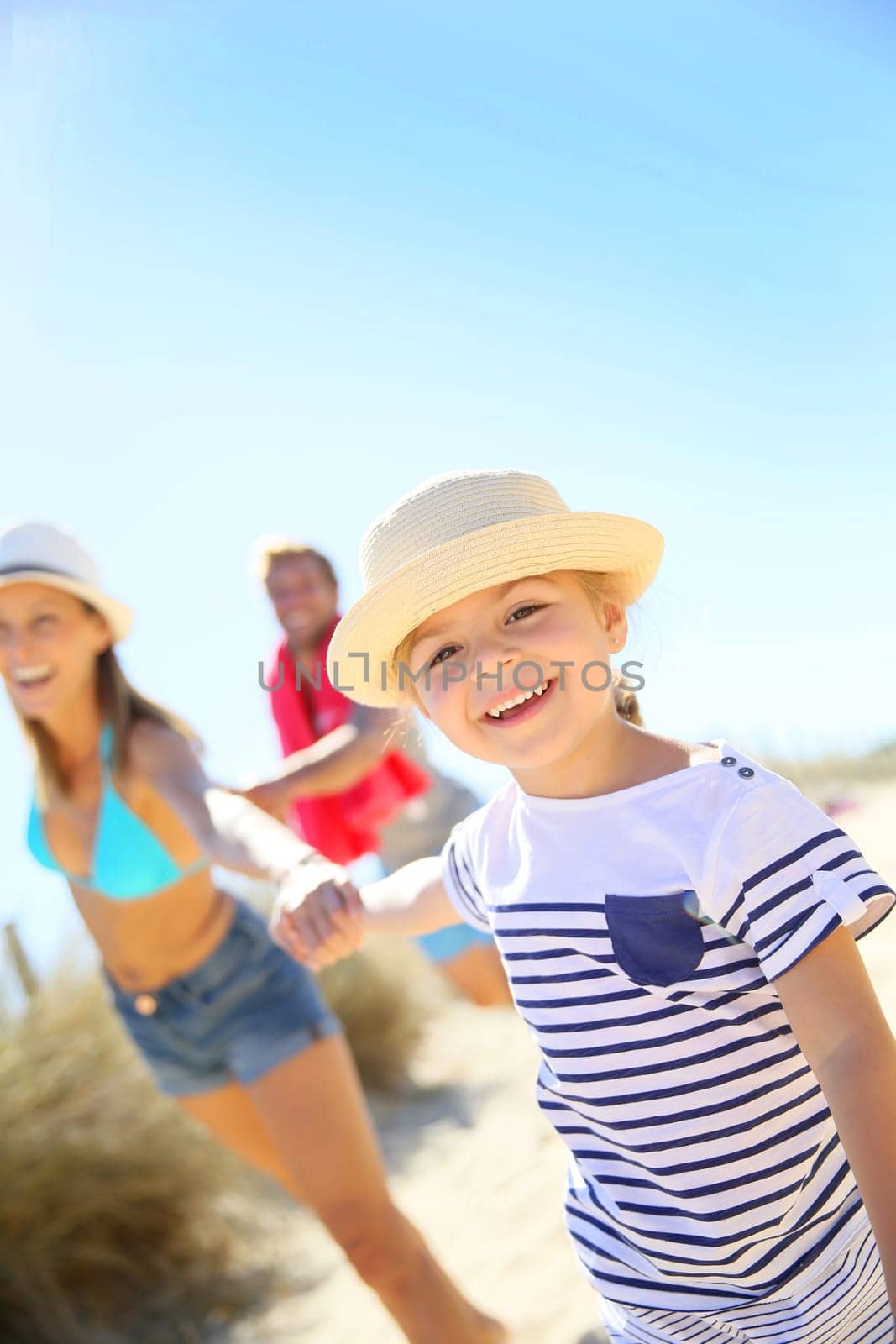 Little girl pulling parents' arms to run to the beach