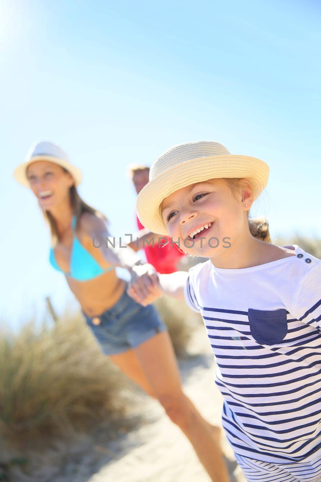Little girl pulling parents' arms to run to the beach