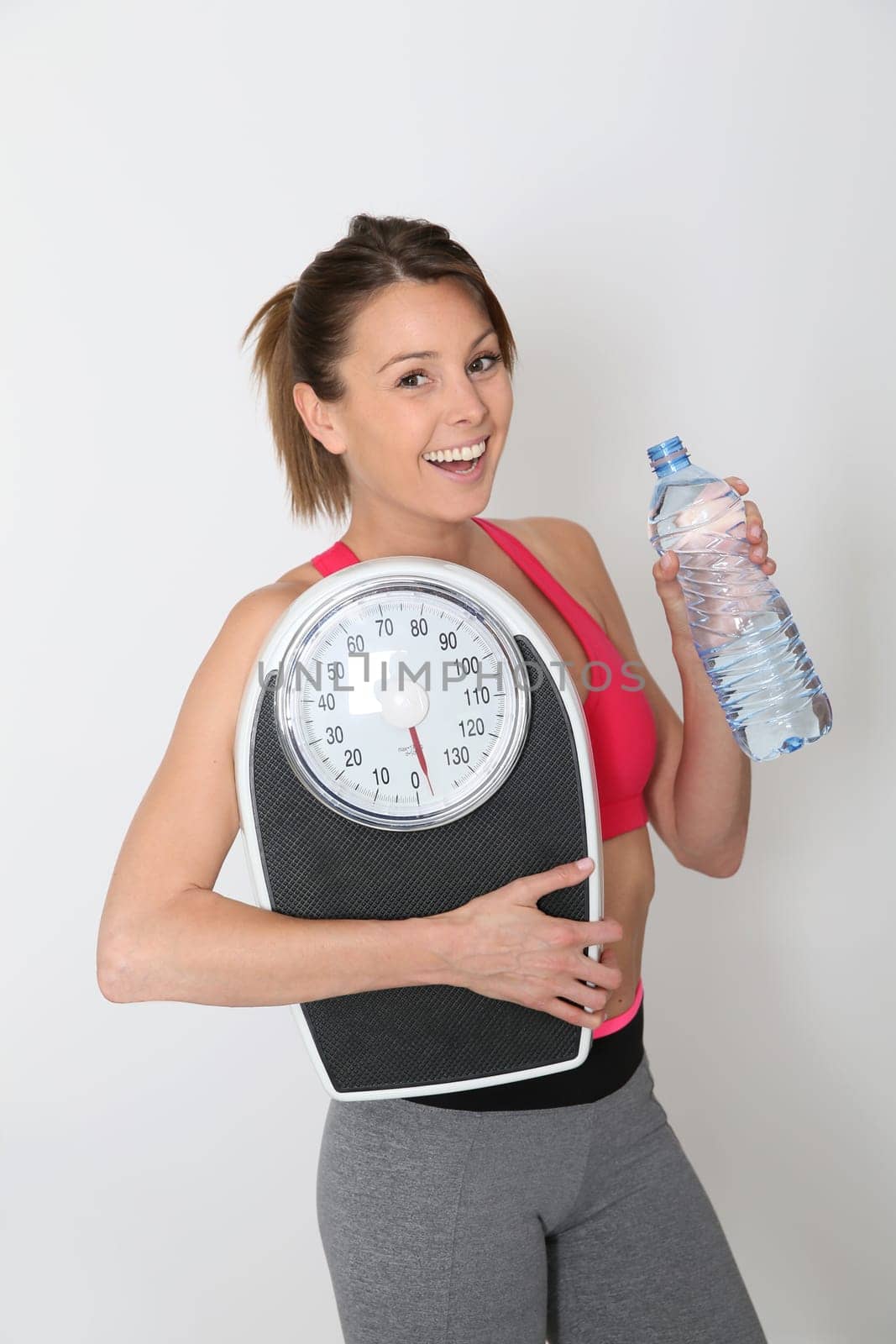 Cheerful fitness girl with bottle of water, holding scale, isolated