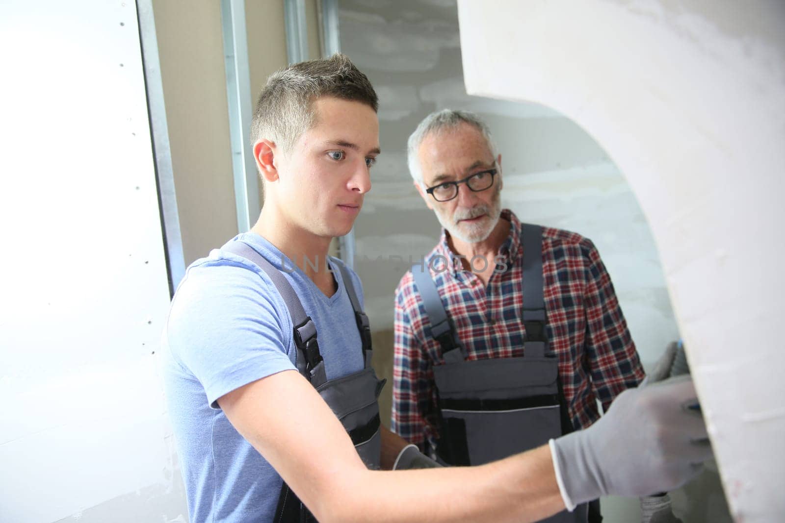 Young apprentice with professional plasterer