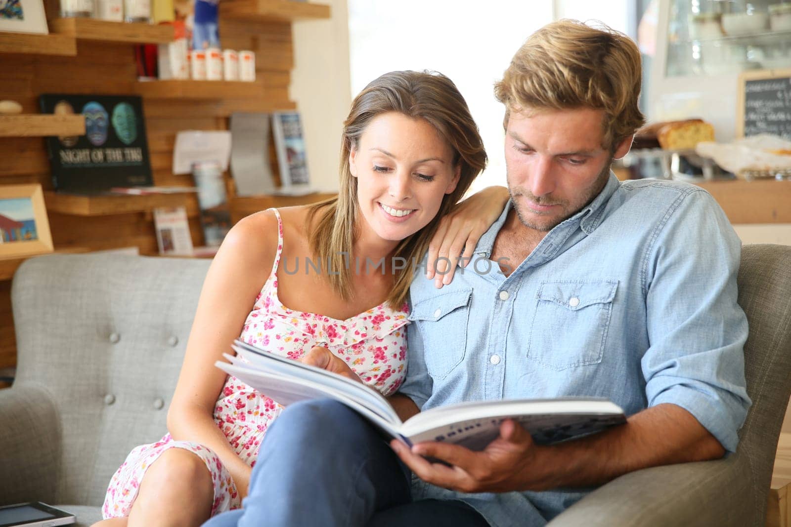 Trendy couple in coffee shop reading magazine sitting in sofa