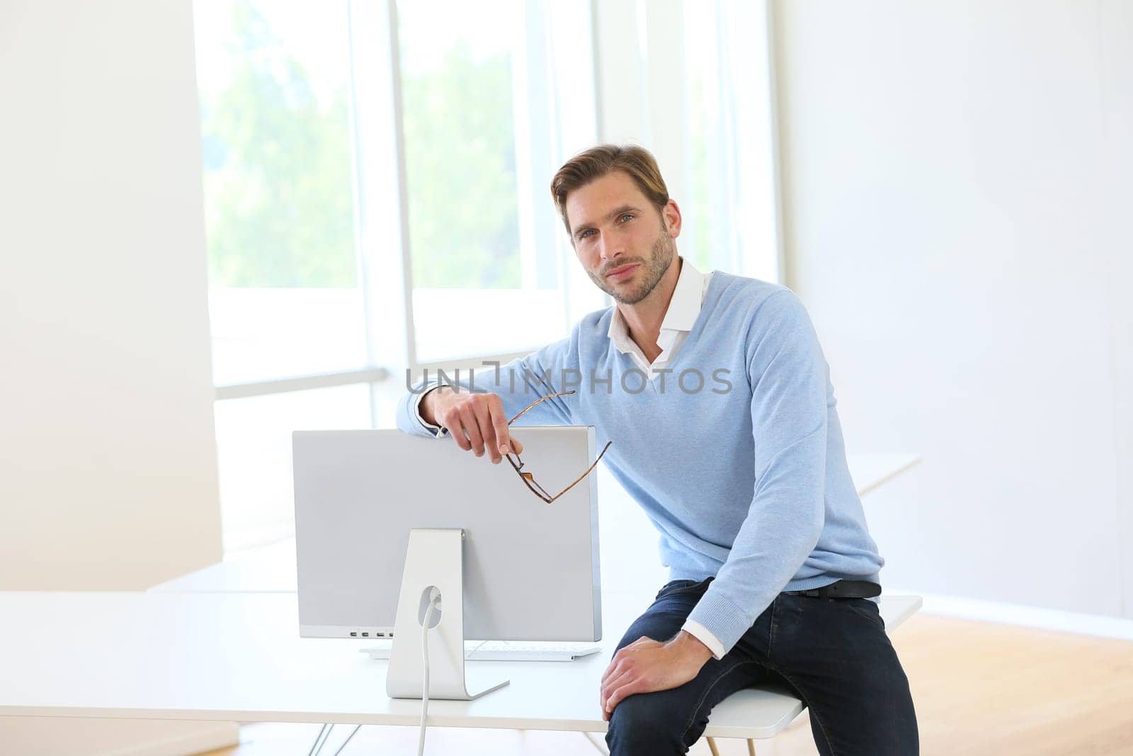 Businessman sitting on table by computer in modern room