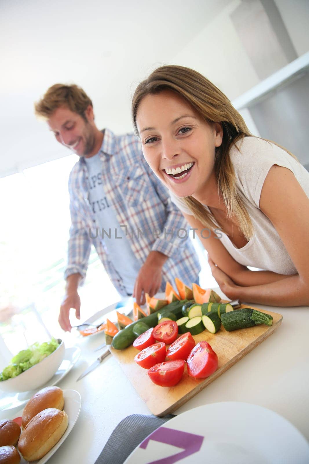 Portrait of cheerful woman in kitchen, boyfriend preparing lunch