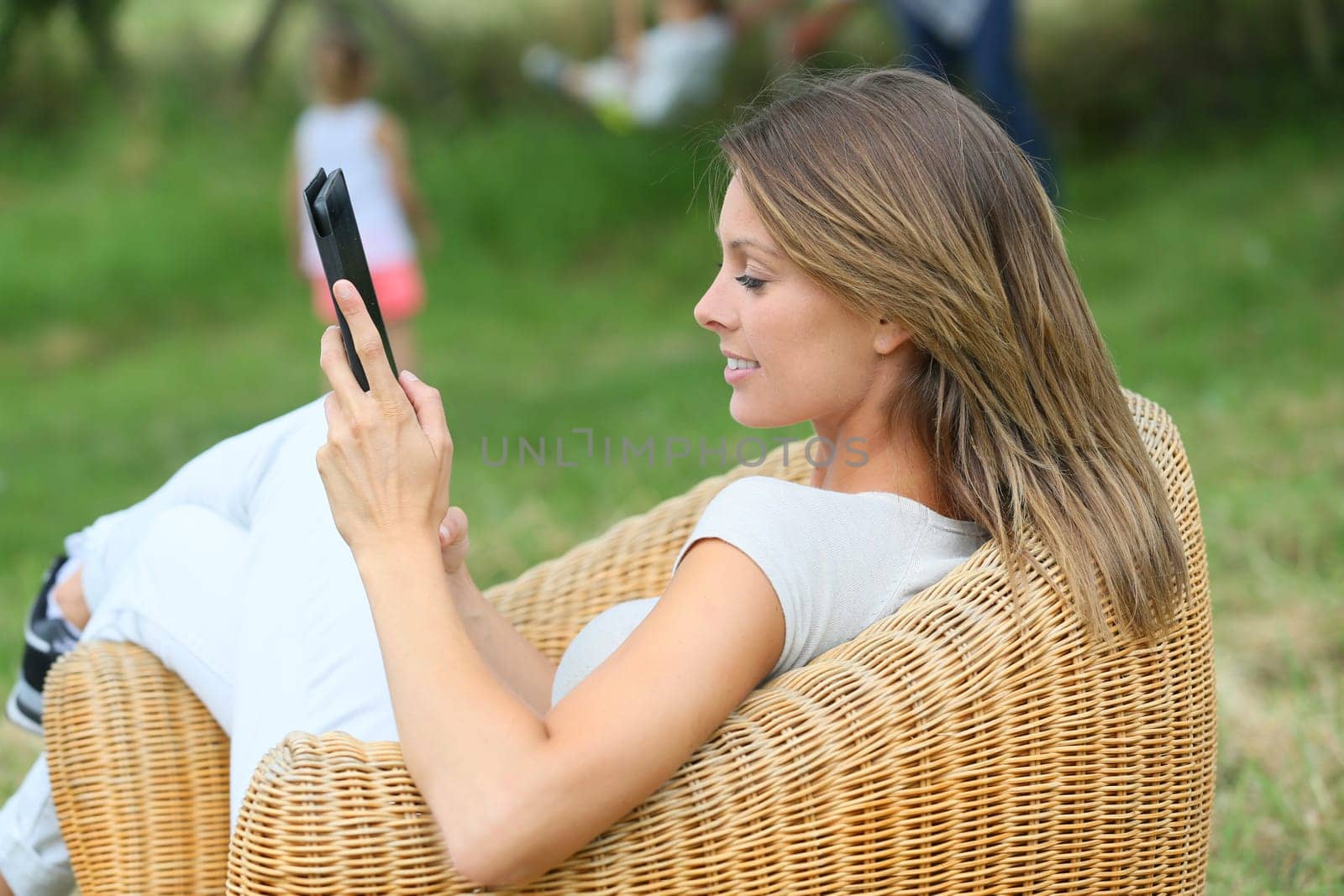 Woman relaxing in outdoor armchair and using digital tablet