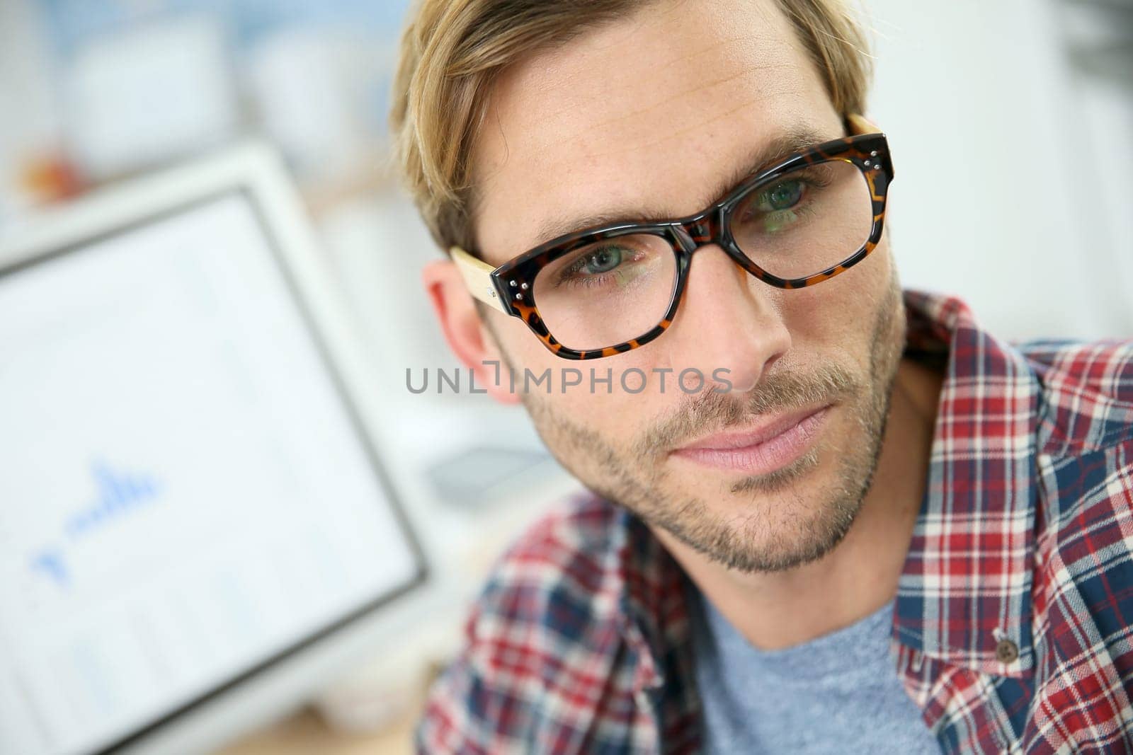 Trendy guy with eyeglasses sitting in office in front of desktop computer