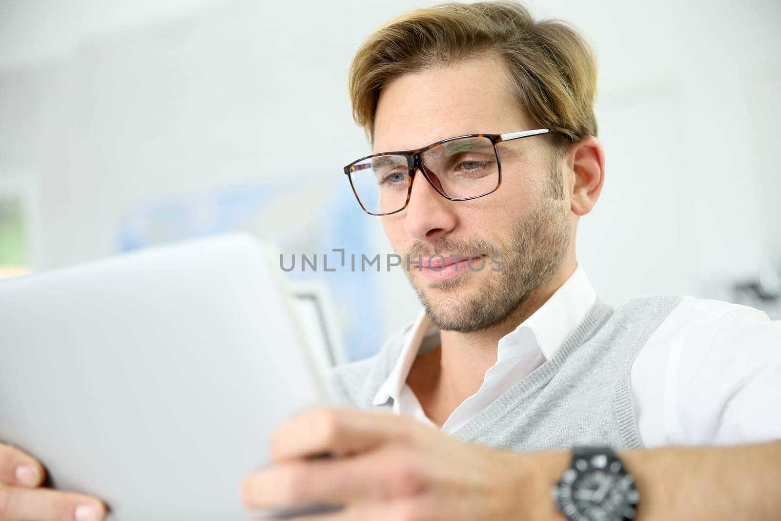 Man in office working on digital tablet, wearing eyeglasses