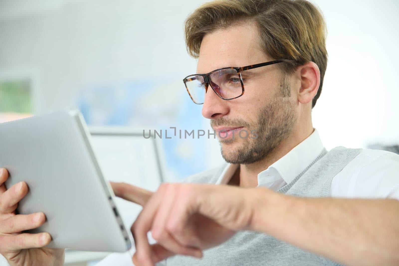 Man in office working on digital tablet, wearing eyeglasses