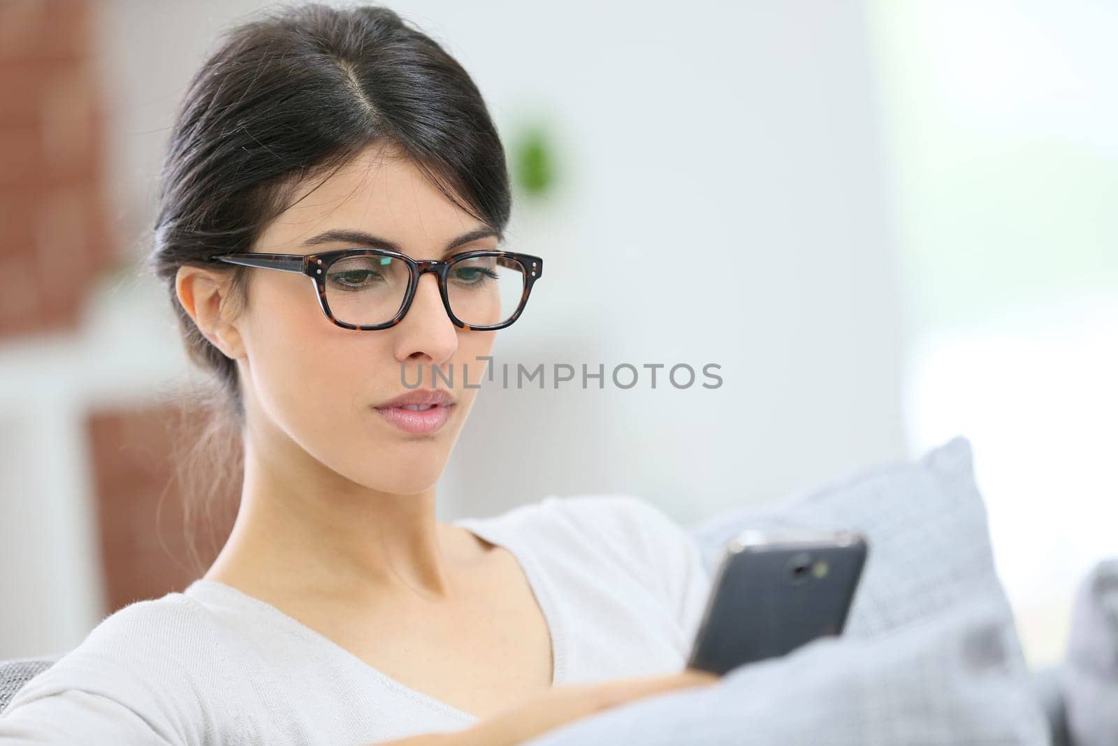 Young woman with eyeglasses reading message on phone