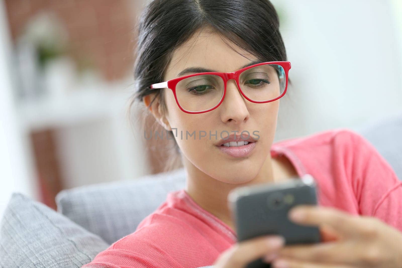 Brunette girl with red eyeglasses reading message on smartphone