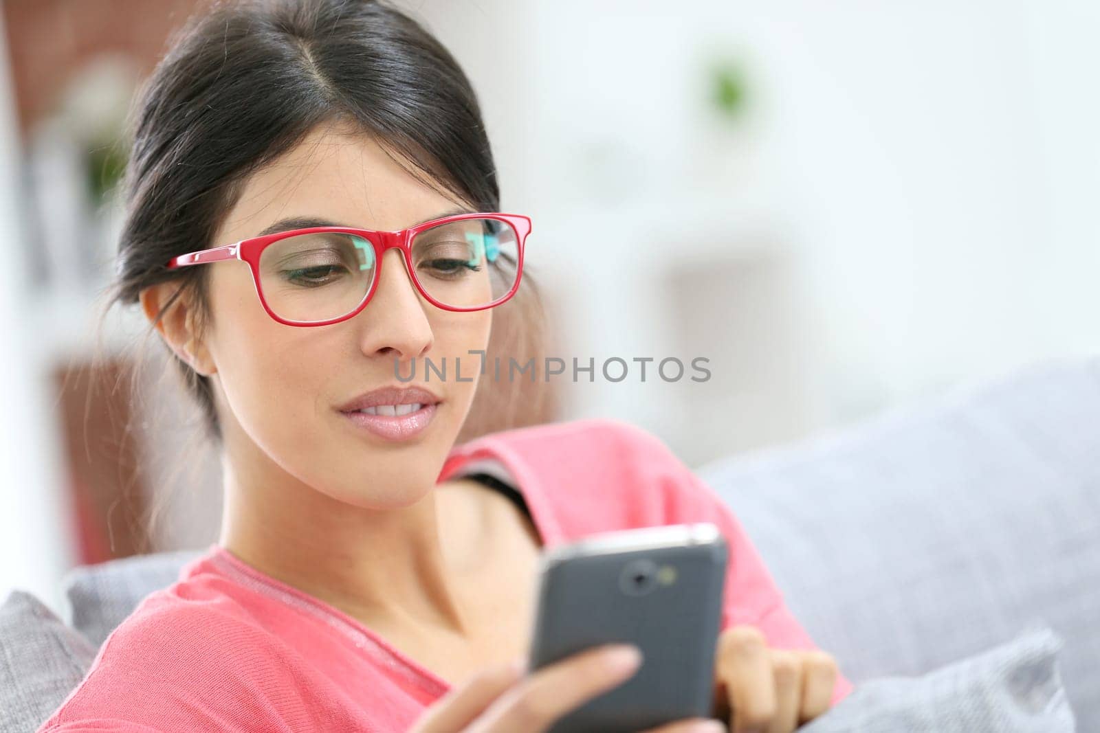 Brunette girl with red eyeglasses reading message on smartphone
