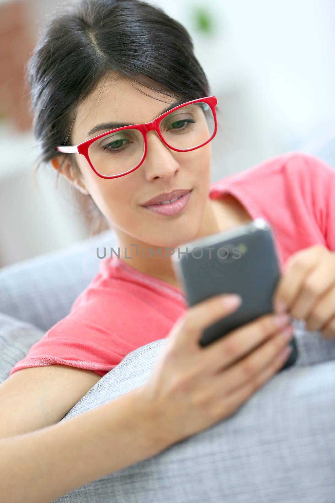 Brunette girl with red eyeglasses reading message on smartphone