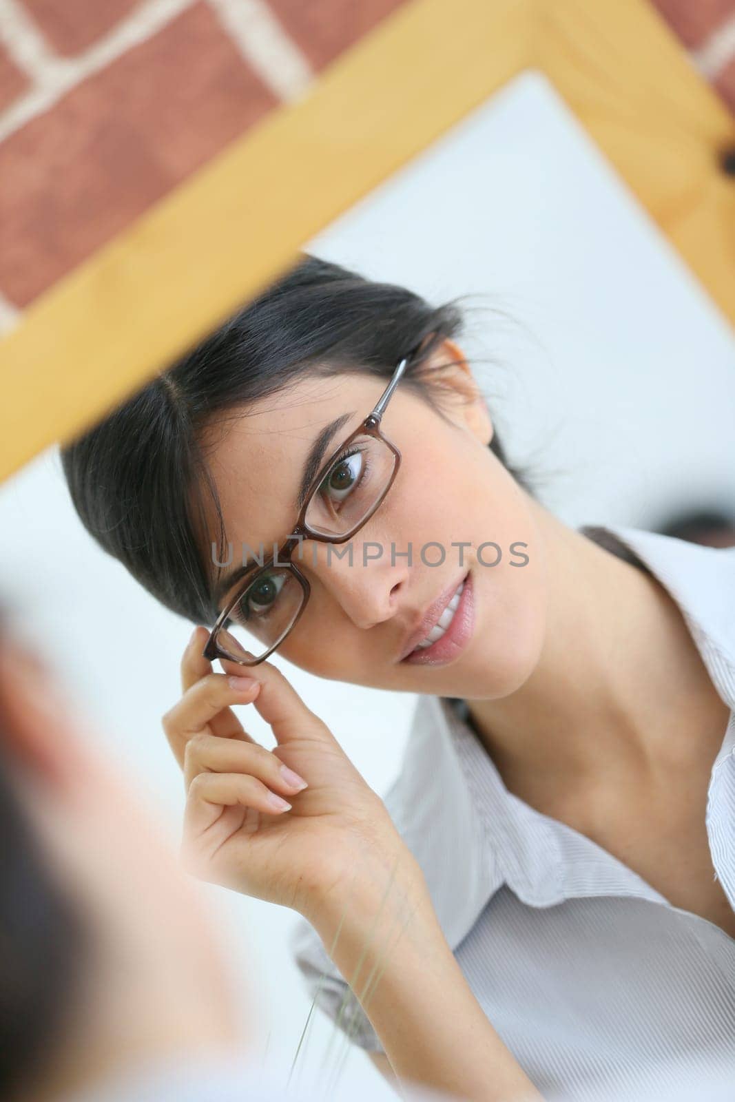Portrait of young brunette woman trying eyeglasses on