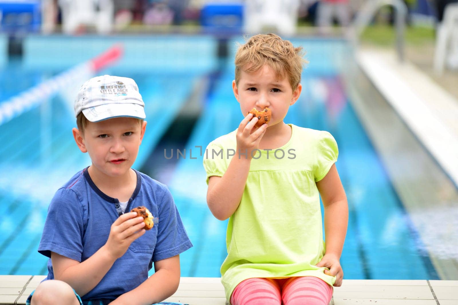 Boy and girl sit at the edge of the pool and eat a muffin