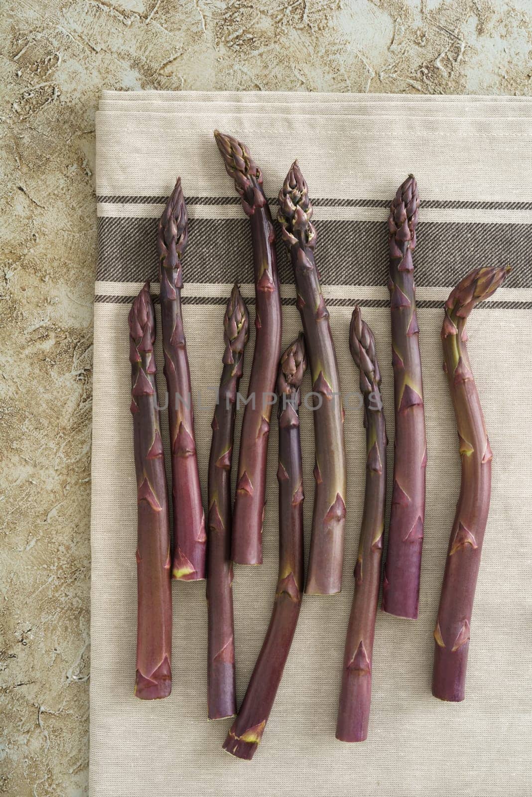 Fresh uncooked purple asparagus stalks on linen cloth