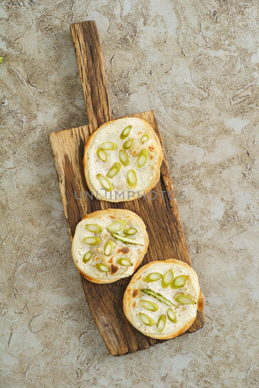 Three mini green asparagus tarte flambee on rustic wooden bards