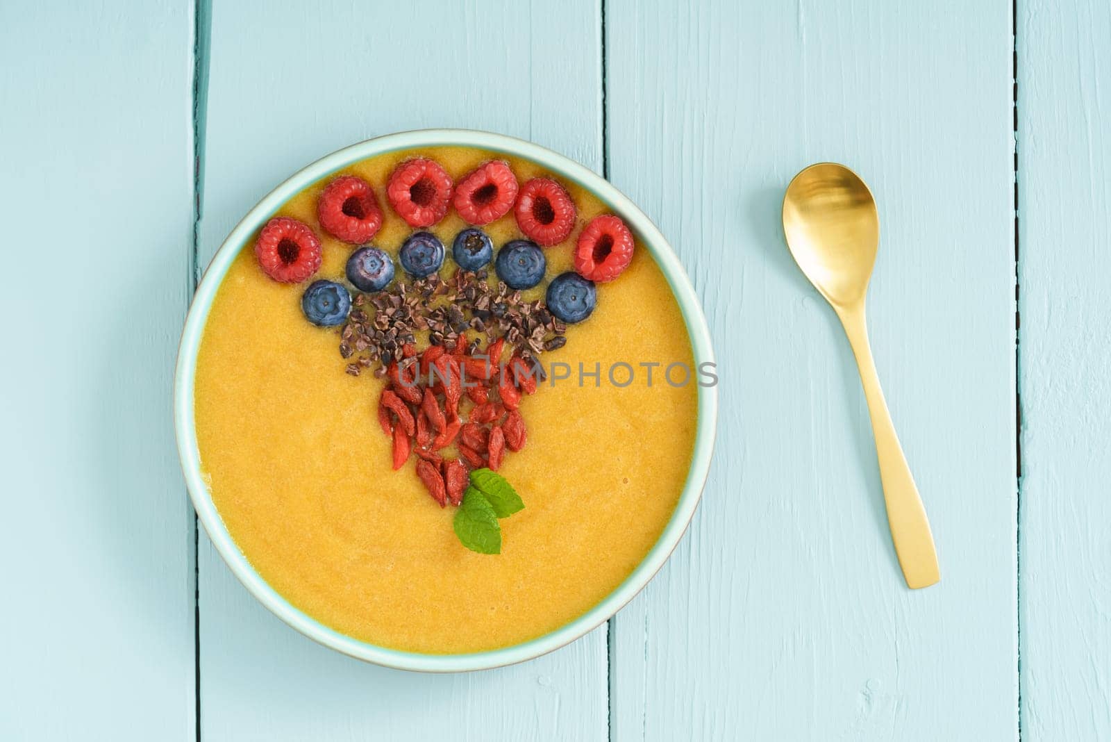 Peach smoothie bowl with blueberries, goji berries, cocoa nibs and raspberries in a bowl