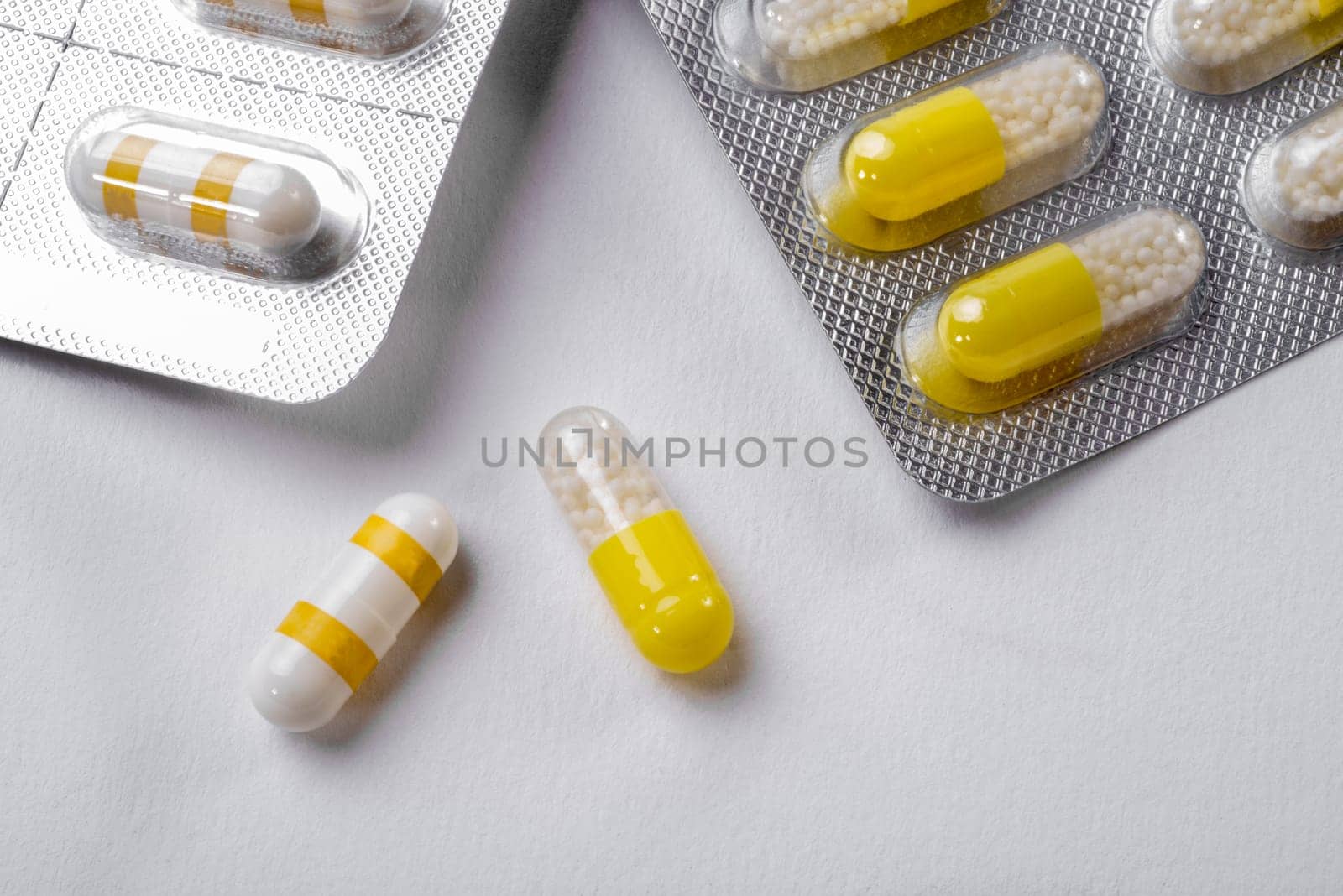 Two white and yellow capsules lie on a white background near by their packaging.