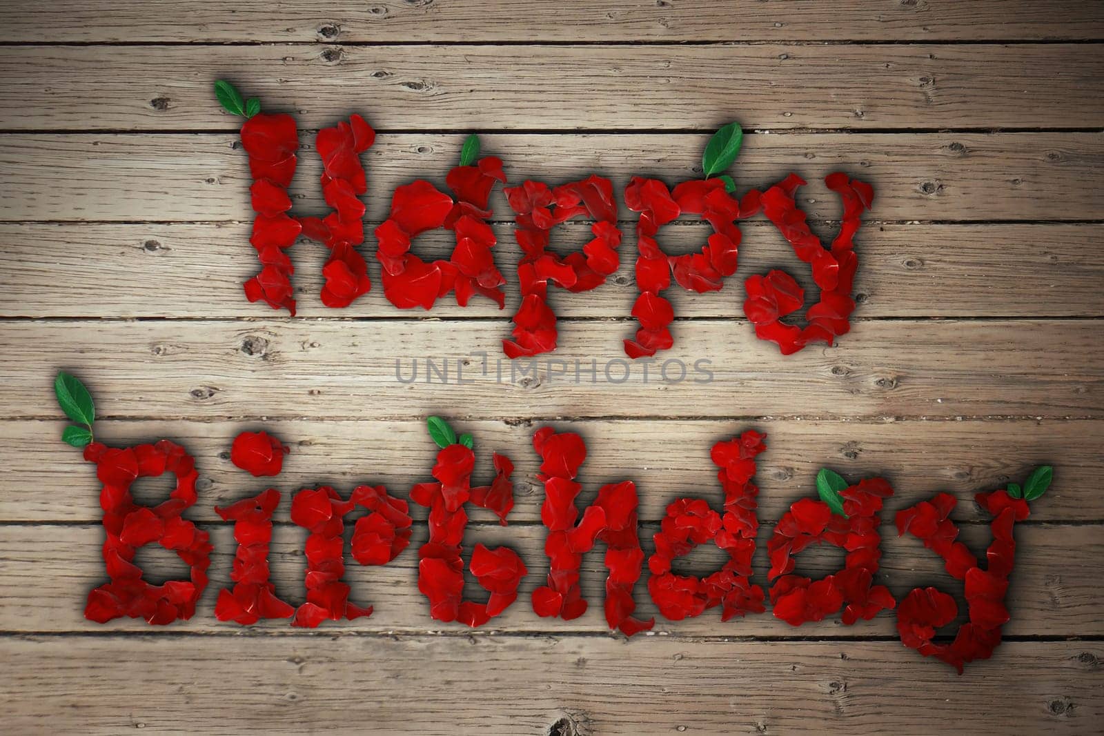 Happy birthday message of red rose petals on wooden table.