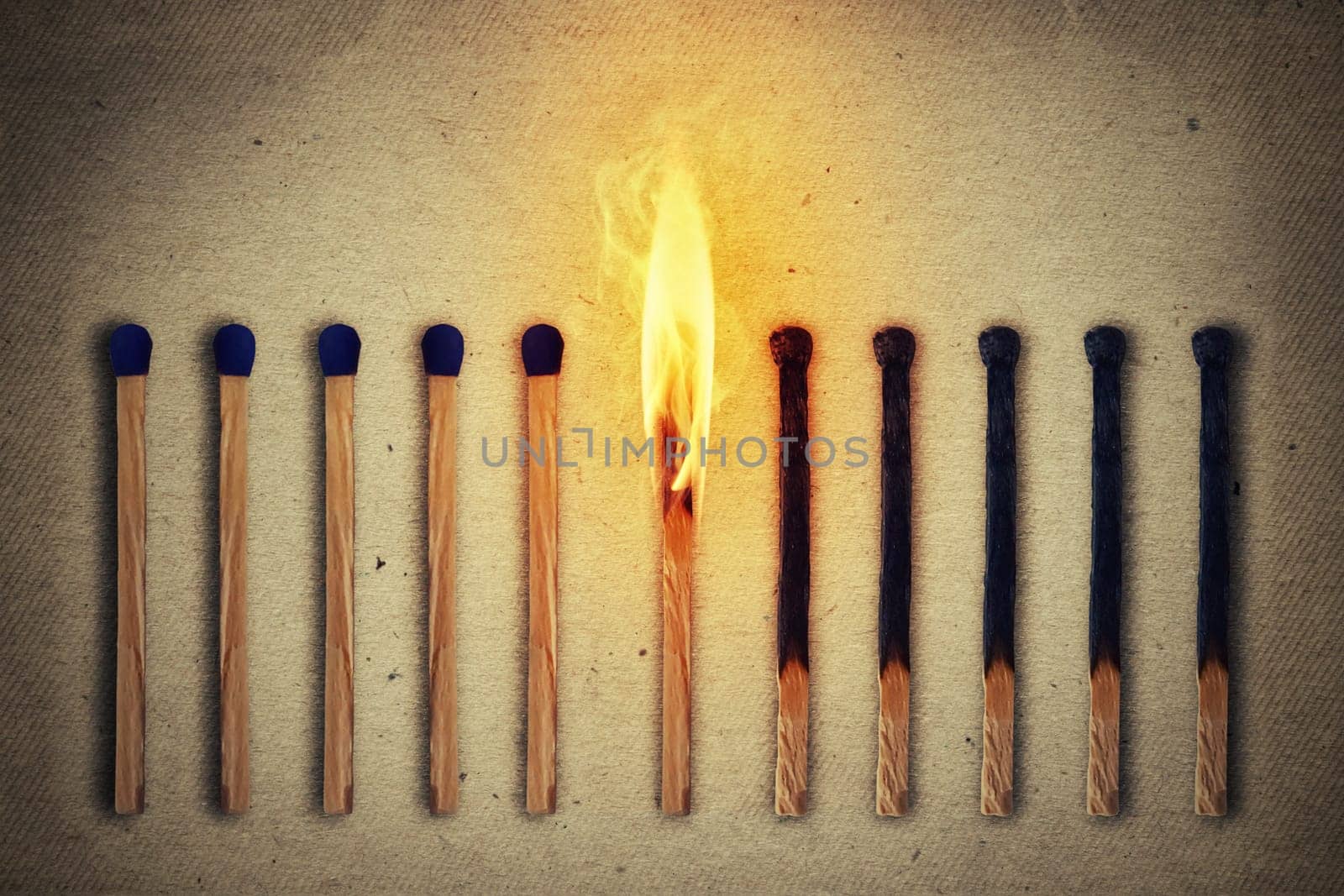 Burning match standing middle a row of whole, new matches at left and extinguished at right. Leadership concept