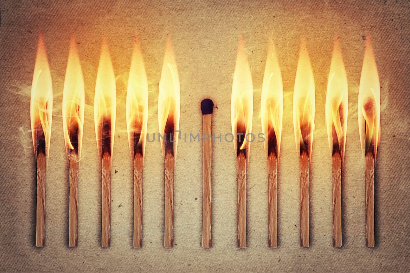 Whole, unused match standing middle a row of burning matches. Standing out from the crowd, leadership concept