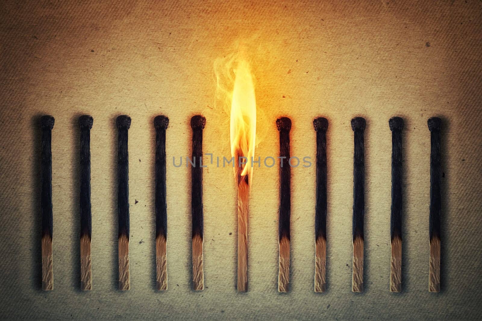 Burning match standing middle a row of extinguished, burnt matches. Leadership concept