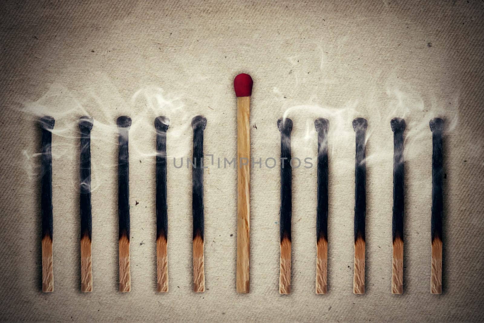 Whole, unused match standing middle a row of extinguished, burnt matches. Standing out from the crowd, leadership concept