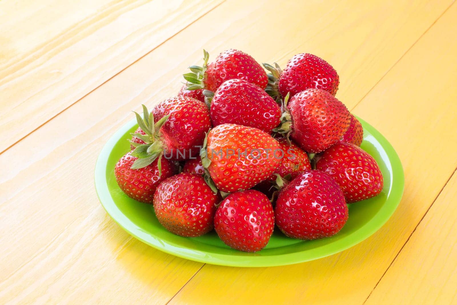 Plate with red strawberries on yellow wooden background.