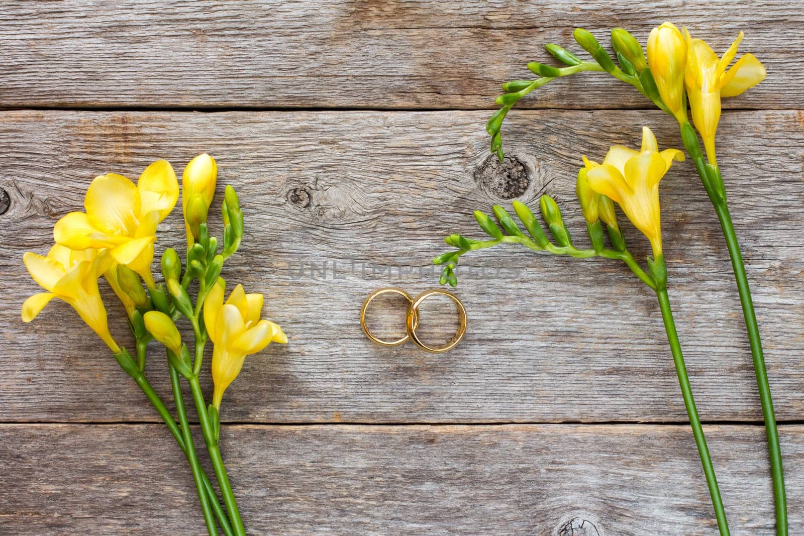 Wedding rings and freesia flowers on wooden background. Top view.