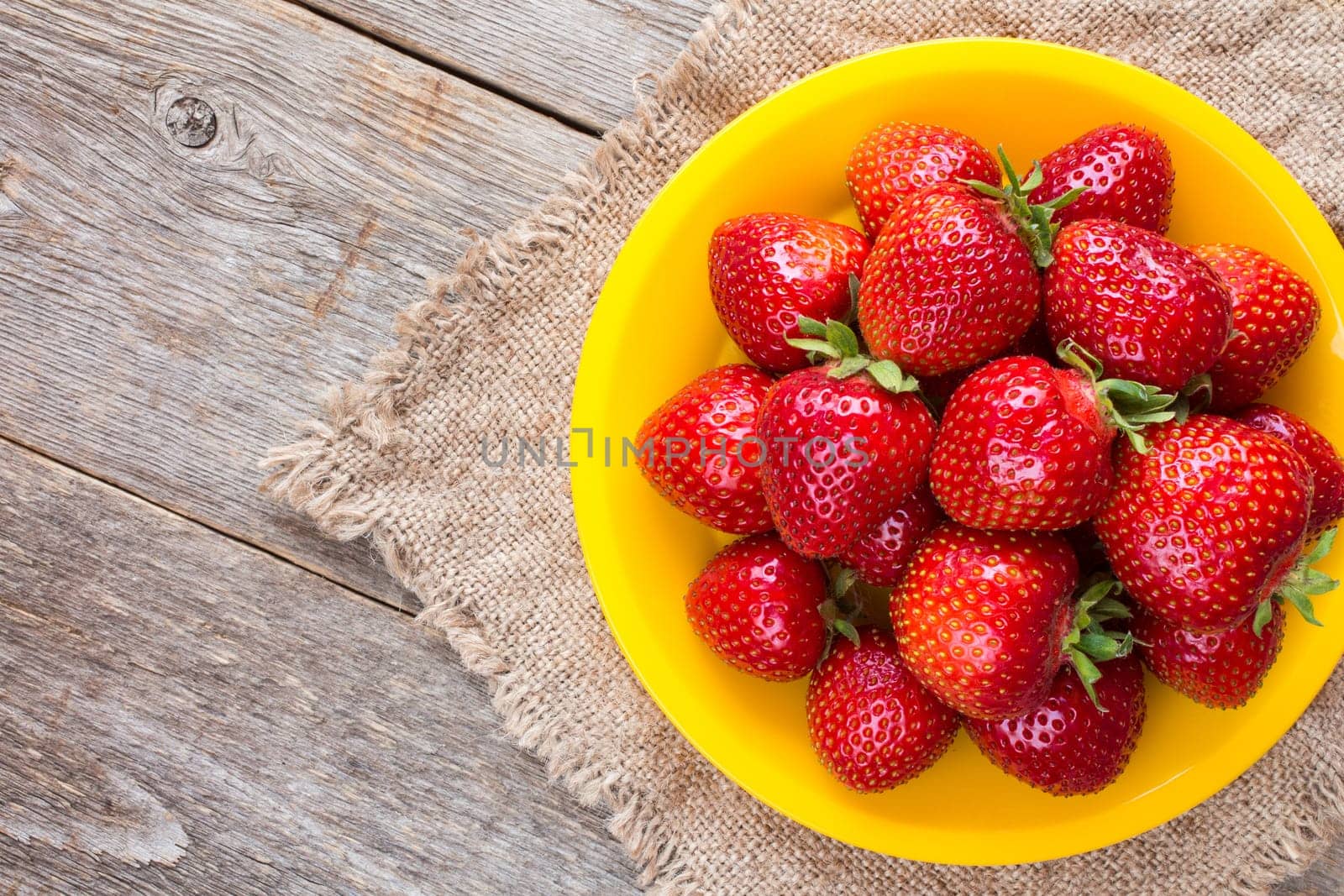 Yellow plate with strawberries on piece of sackcloth