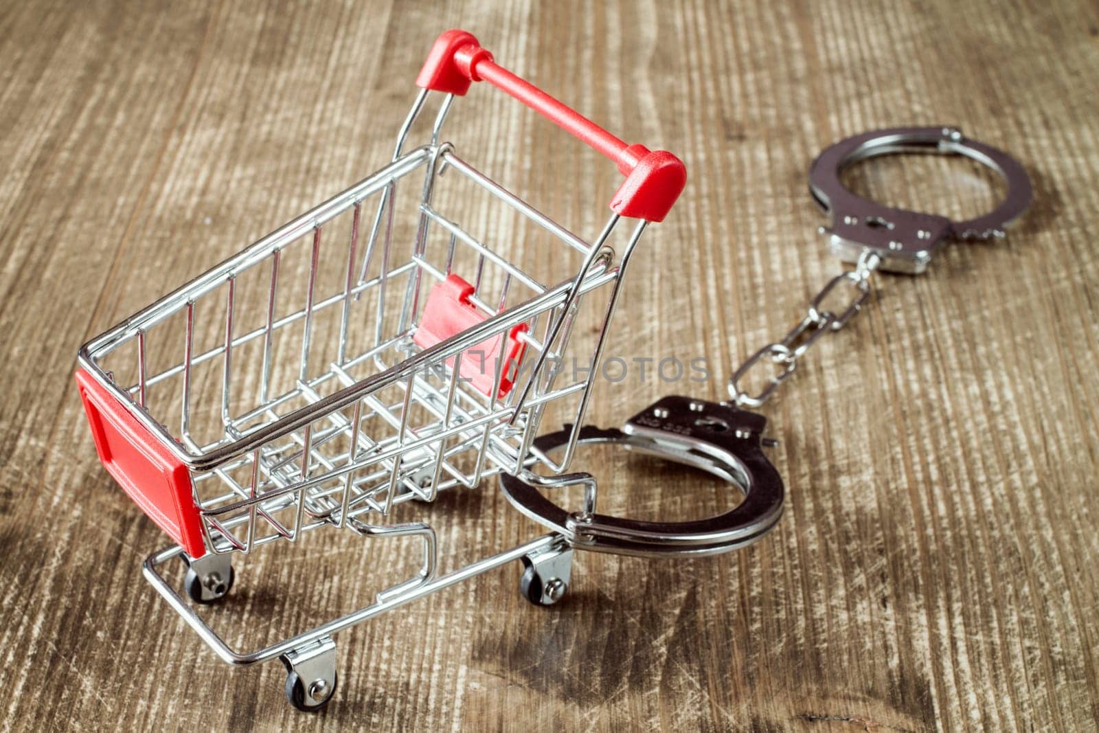 Shopping cart and handcuffs on old wooden background