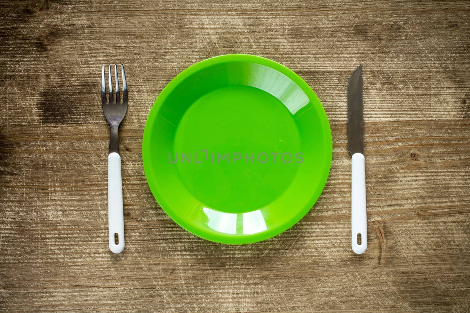 Empty plate, fork and knife on wooden background. Top view with text space