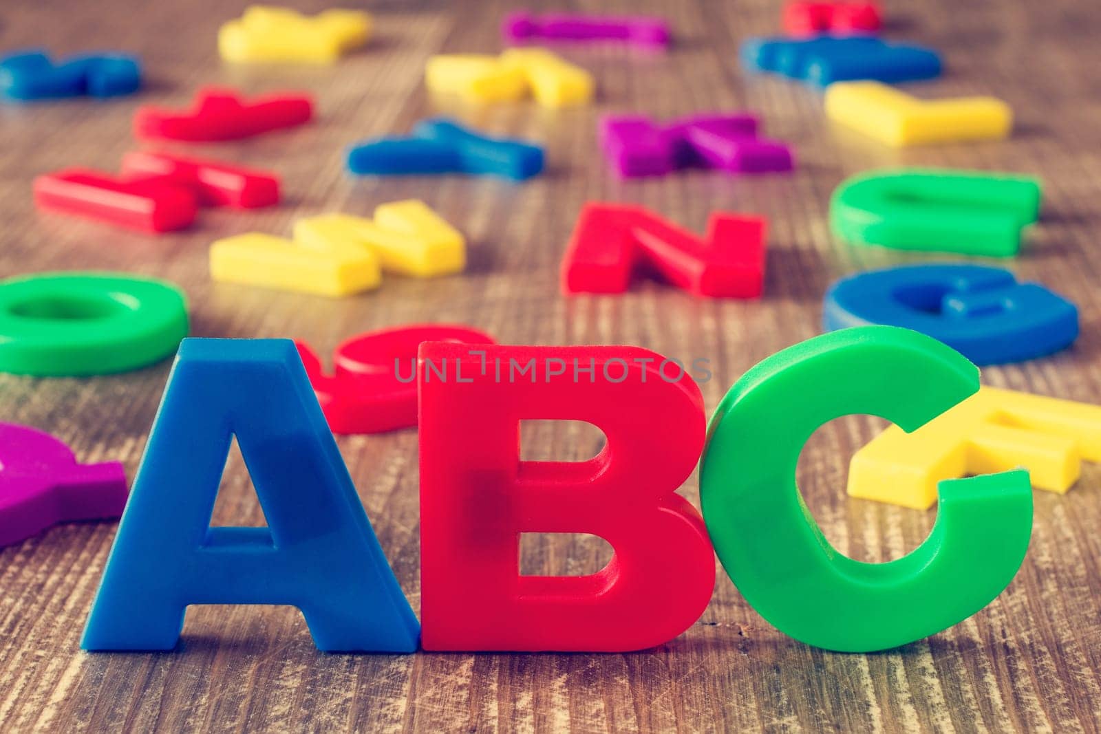 ABC spelling and pile of colorful plastic letters on wooden background