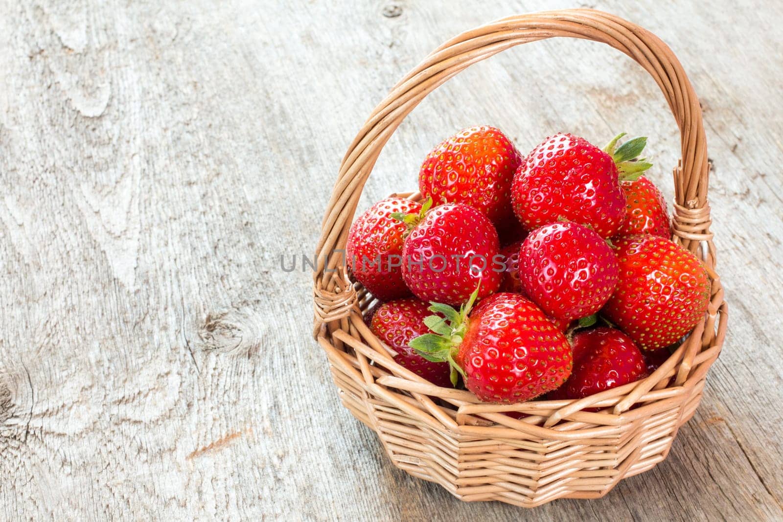 Red strawberries in wicker basket on a wooden background