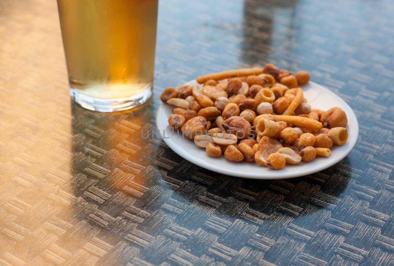 Cold glass of beer over terrace table with snack of dried fruit and nuts