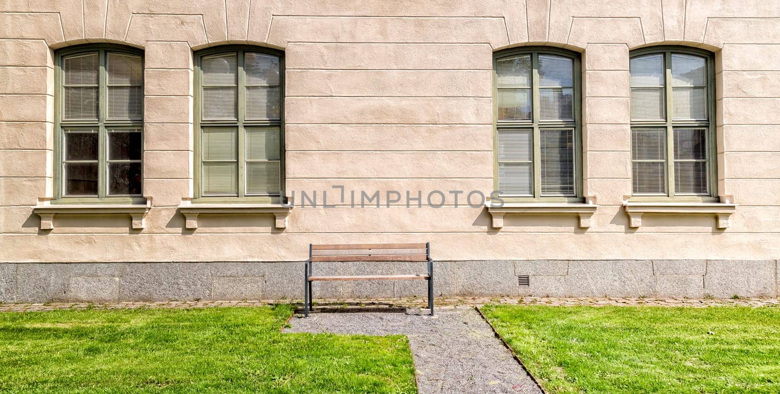 Bench in front of Windows on building with grass.