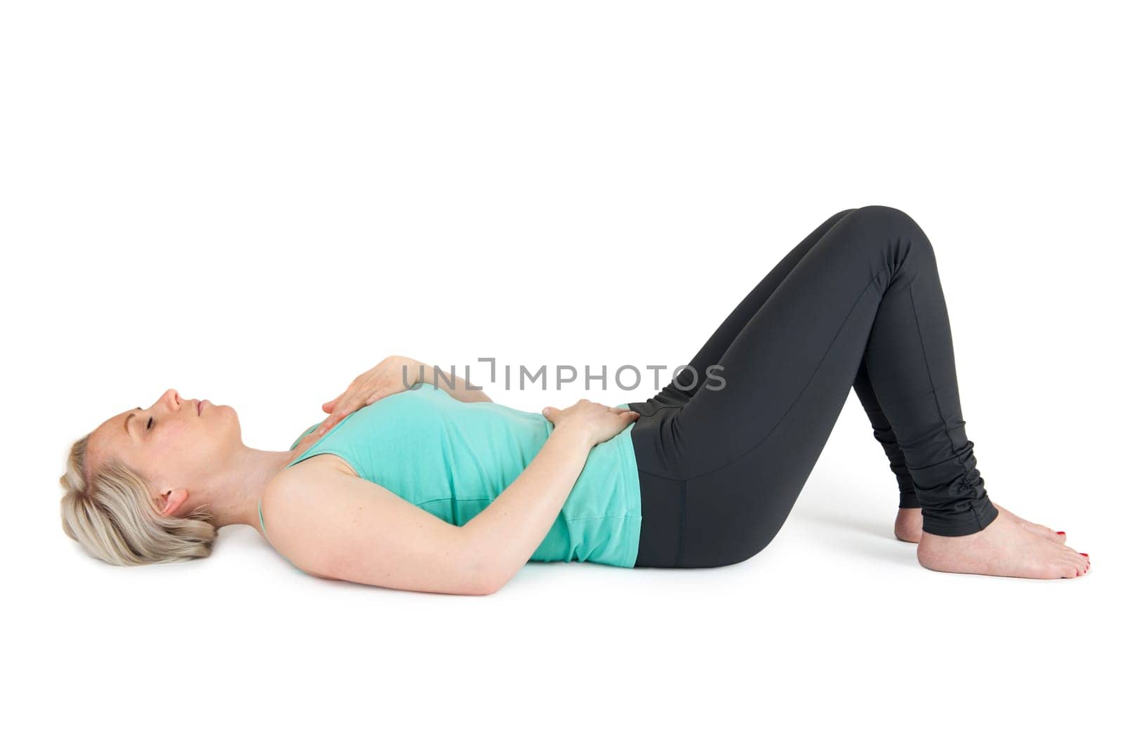 Full body view of a young blonde woman doing yoga exercises against a white background with a slight shadow
